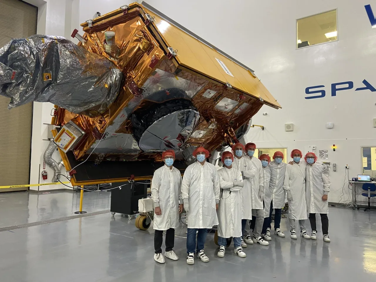 A team in cleanroom clothing stands beside the gold-covered Sentinel-6 Michael Freilich spacecraft.
