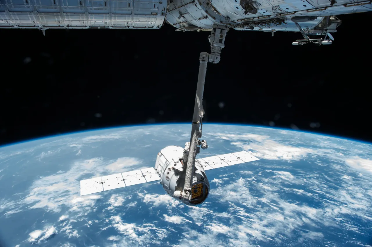 Canadarm2 holds a Dragon cargo spacecraft with extended solar arrays above Earth