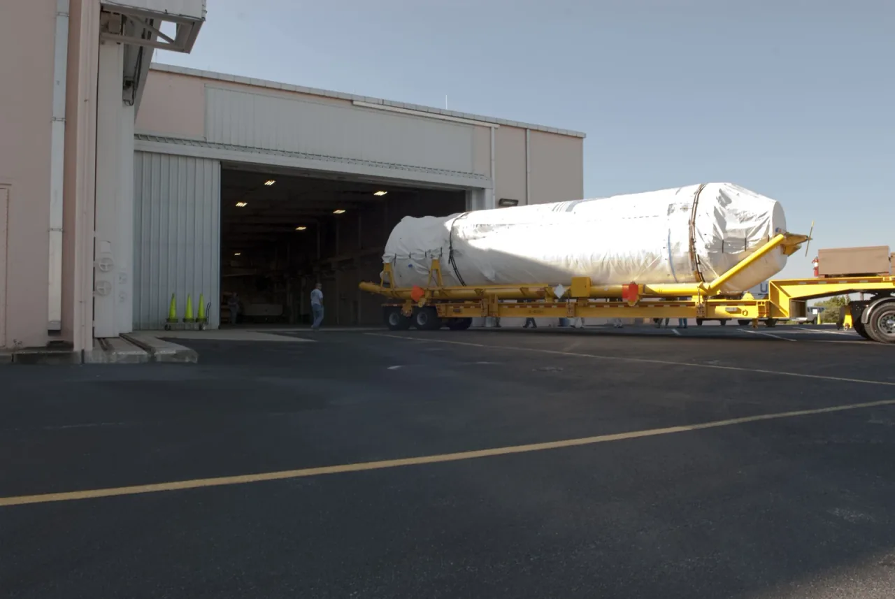 A covered Centaur upper stage on a transporter outside a processing building