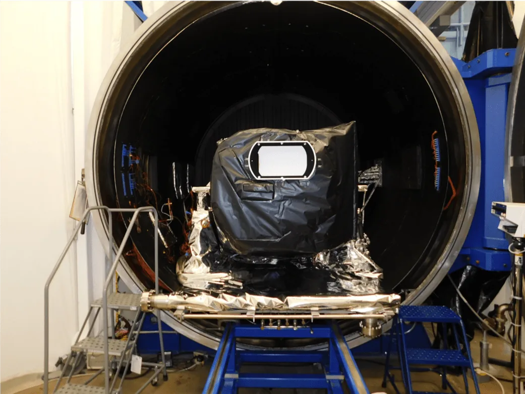 A black-covered TEMPO instrument with a light rectangular opening sits on a blue support frame in front of a large circular test chamber.