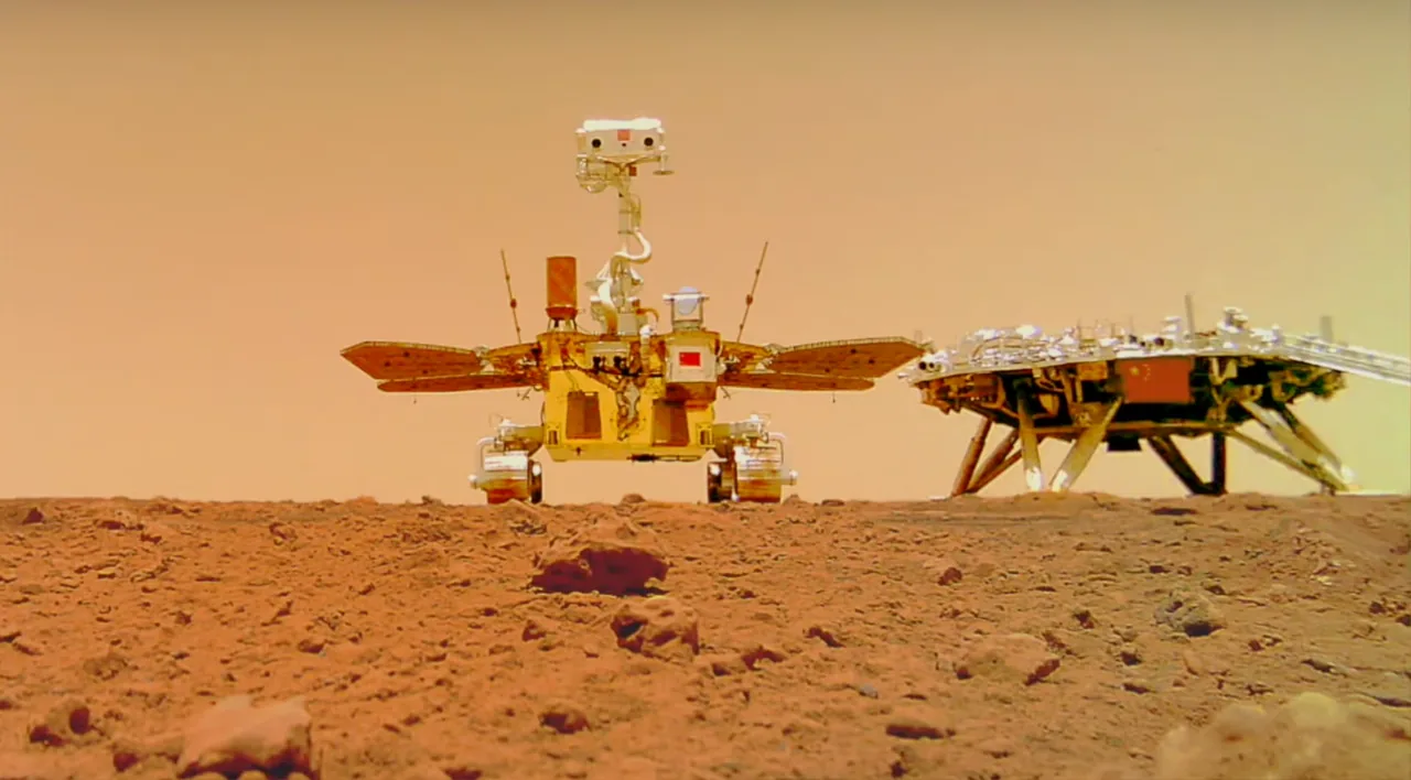Zhurong faces a ground-level camera with its solar wings extended, while the Tianwen-1 landing platform stands to the right.