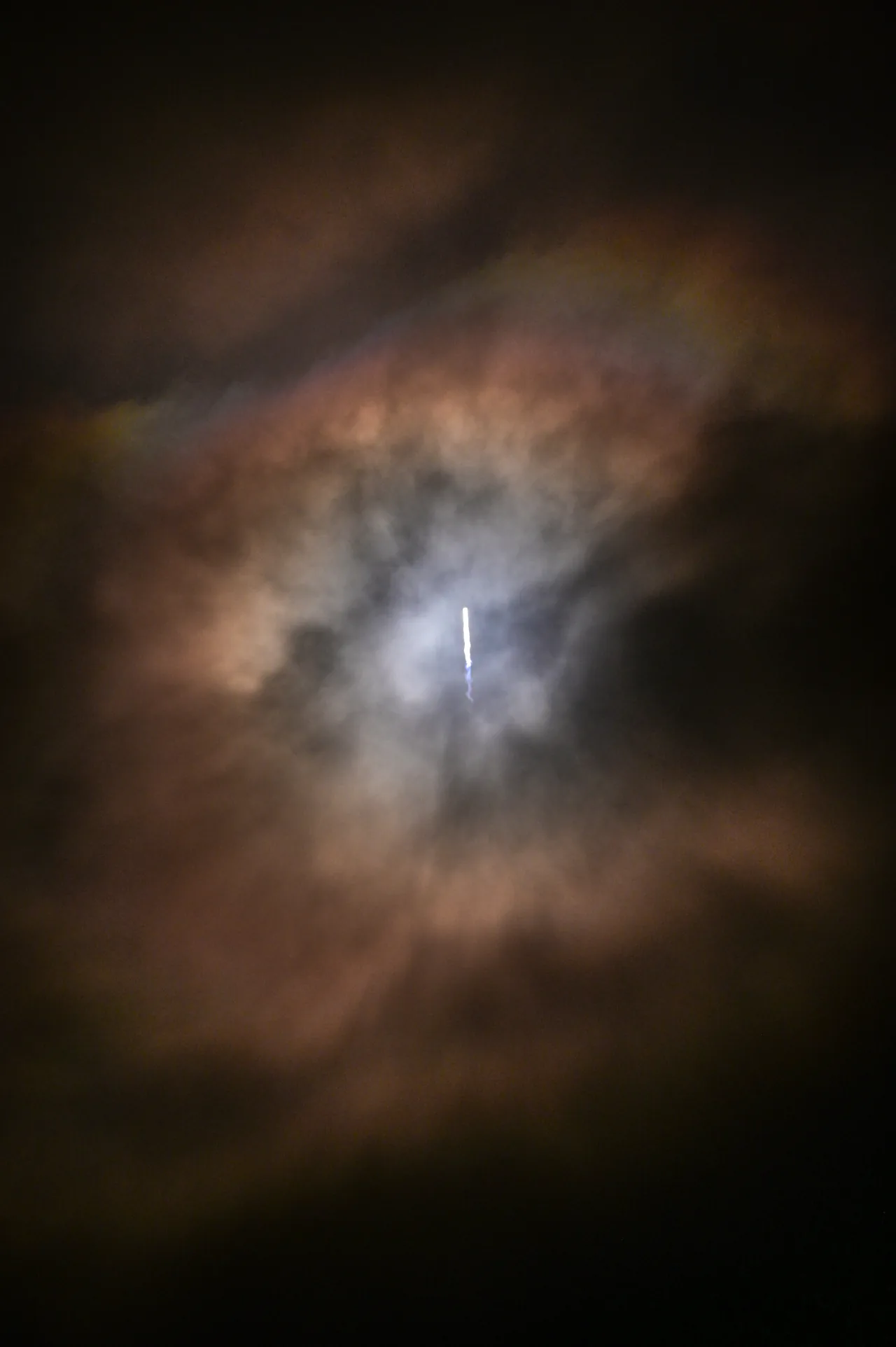 The Transporter-7 launch appears as a bright rising streak at the center of a glowing opening in dark night clouds.