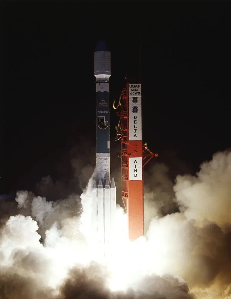 A Delta II rocket marked WIND lifts off at night amid bright exhaust and white clouds