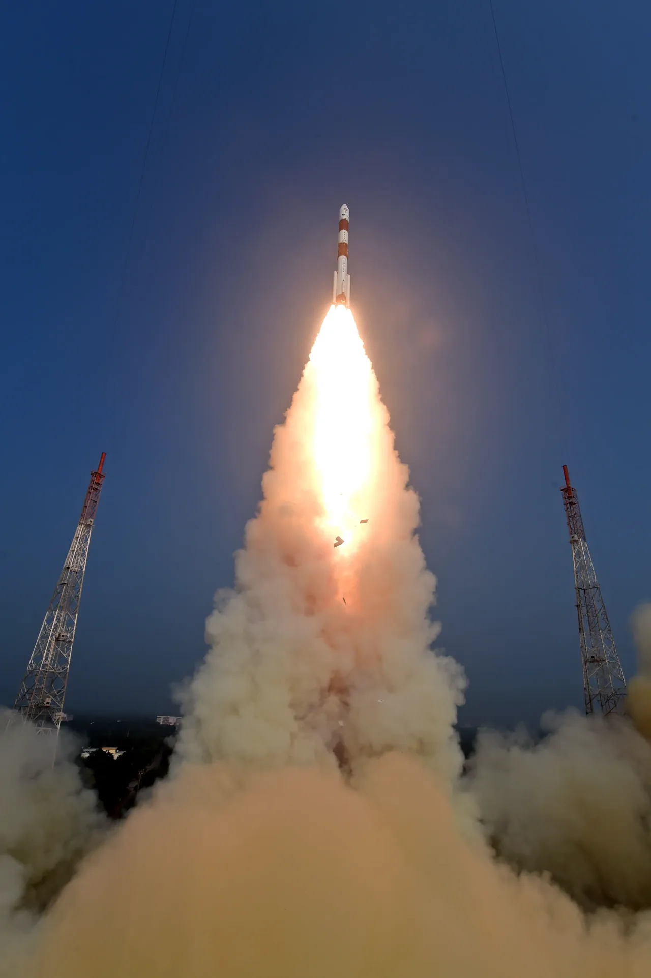PSLV-C58 rises between lightning towers with a brilliant flame and a spreading exhaust cloud