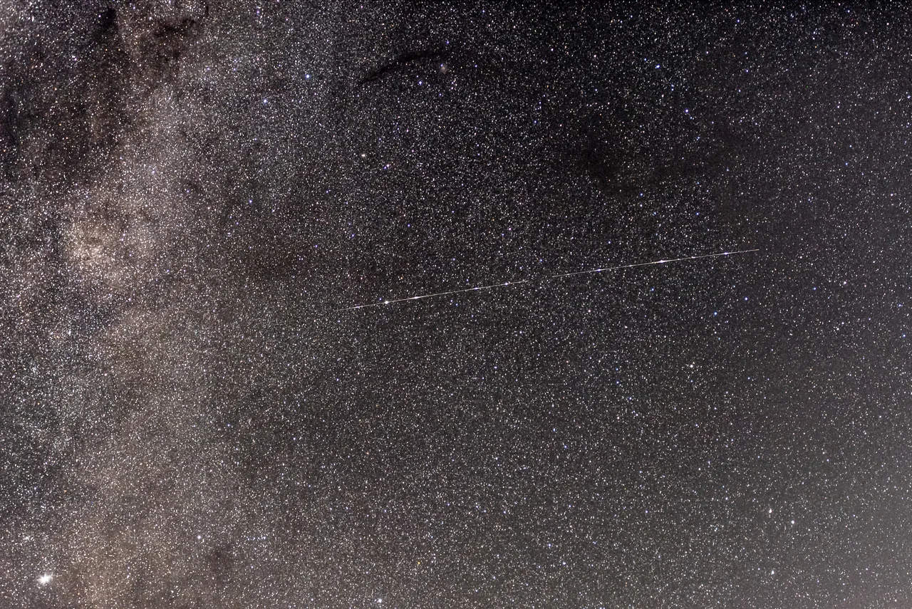 A bright segmented diagonal trail crosses a dense star field in a nighttime exposure.
