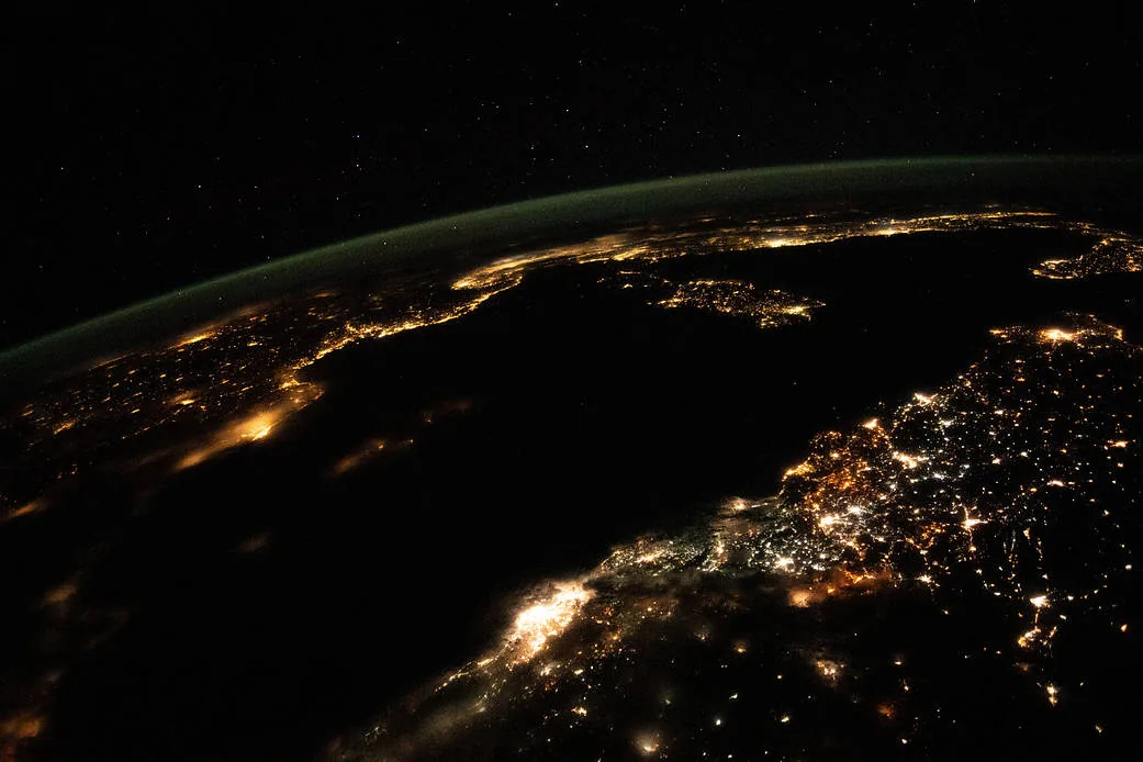 City lights trace Mediterranean coastlines beneath a curved green atmospheric glow in a nighttime view from the International Space Station