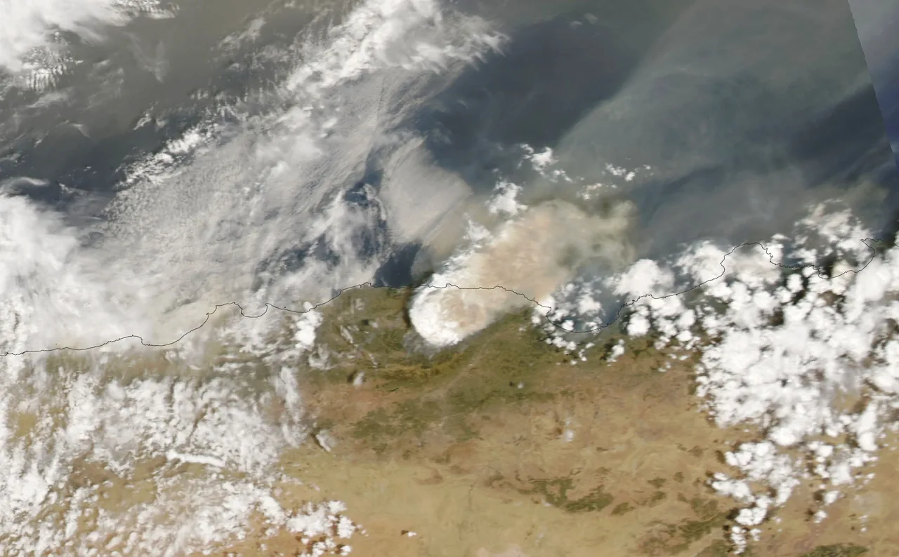 A broad pale smoke plume and white clouds extend above Algeria and the Mediterranean coast