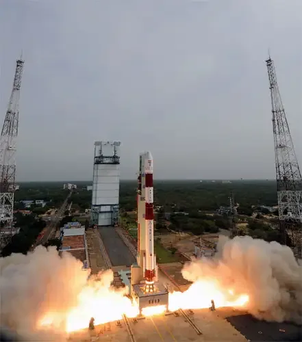 PSLV-C15 rises between launch-pad towers above orange exhaust and a spreading white plume