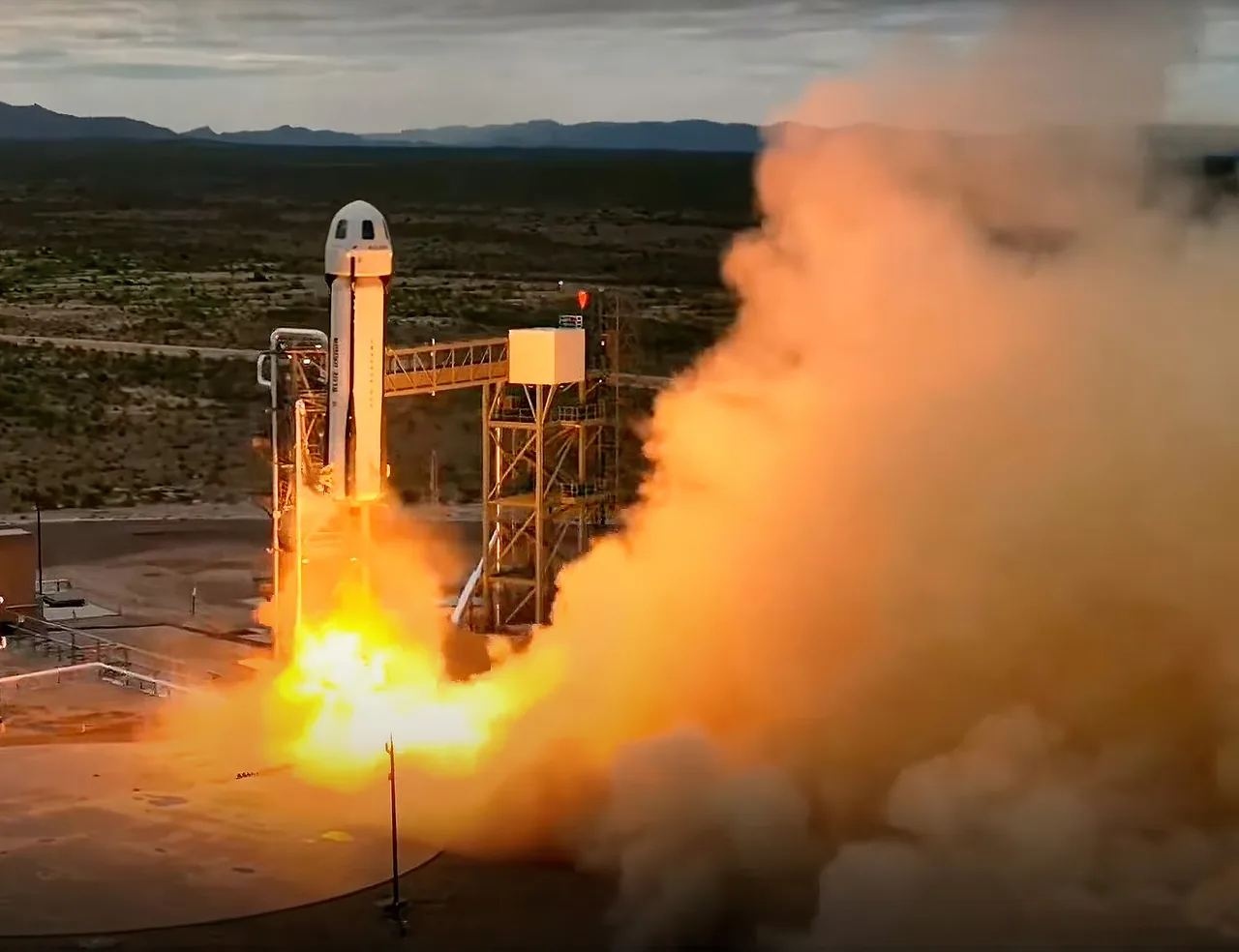 New Shepard lifts off beside its launch tower amid bright exhaust and dust