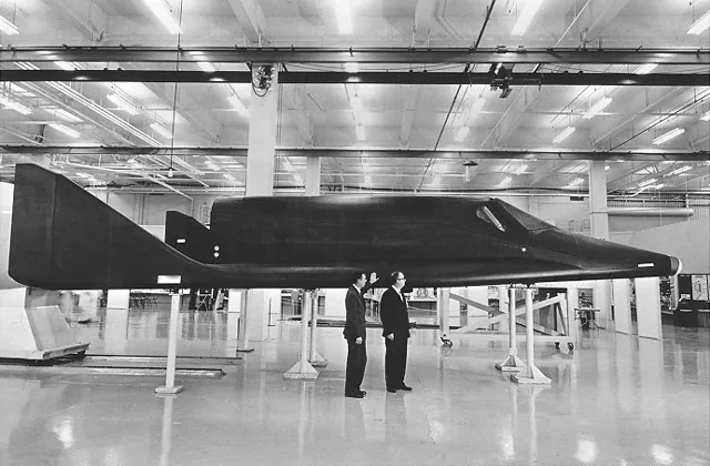 A full-scale X-20 mock-up stands indoors with a pointed nose and compact delta wing