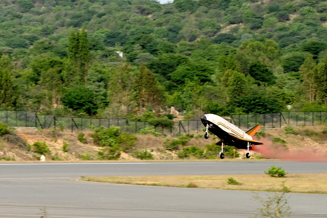 A white and black winged test vehicle with an Indian tricolor stripe approaches a runway with its landing gear extended.