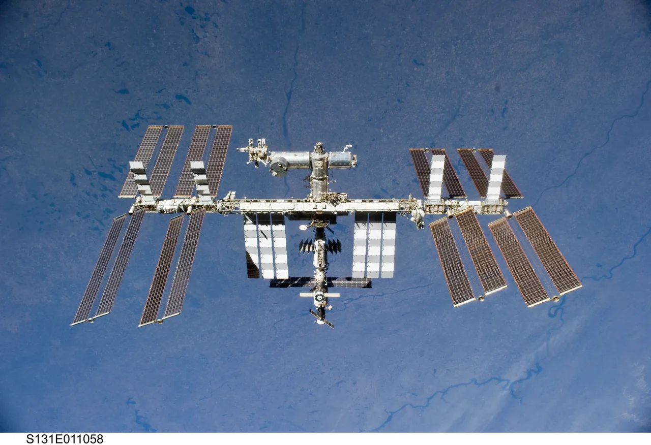 The International Space Station appears above Earth with broad dark solar arrays, pale radiator panels, and modules clustered around its truss.