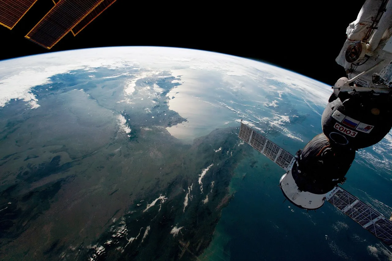 Wide orbital view across Southeast Asia with rivers, cloud bands, sunlit water and the curved horizon, framed by station solar panels and a docked spacecraft
