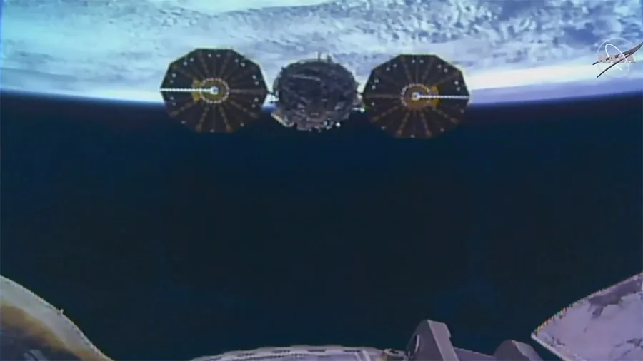 Cygnus with two circular solar arrays beyond station hardware, with Earth across the upper edge