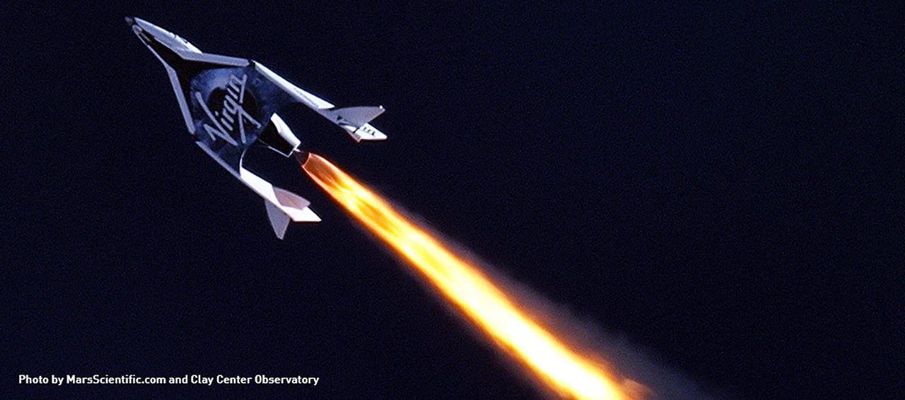 SpaceShipTwo climbs with a long bright rocket plume against a dark sky