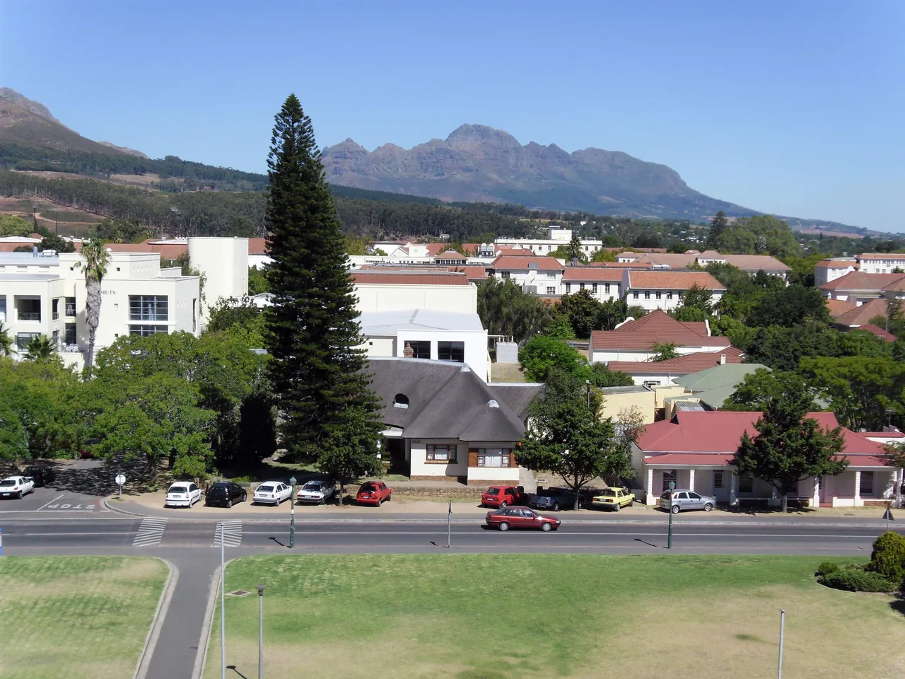 University buildings and trees spread below an elevated viewpoint, with a road in the foreground and mountains beyond
