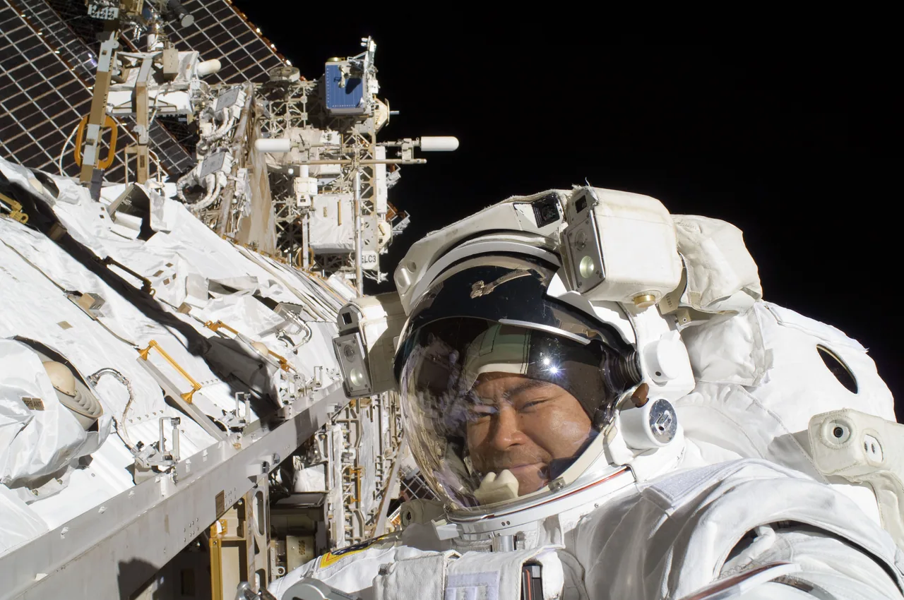 Akihiko Hoshide in a spacesuit beside the station truss, with solar panels and several antennas against black space