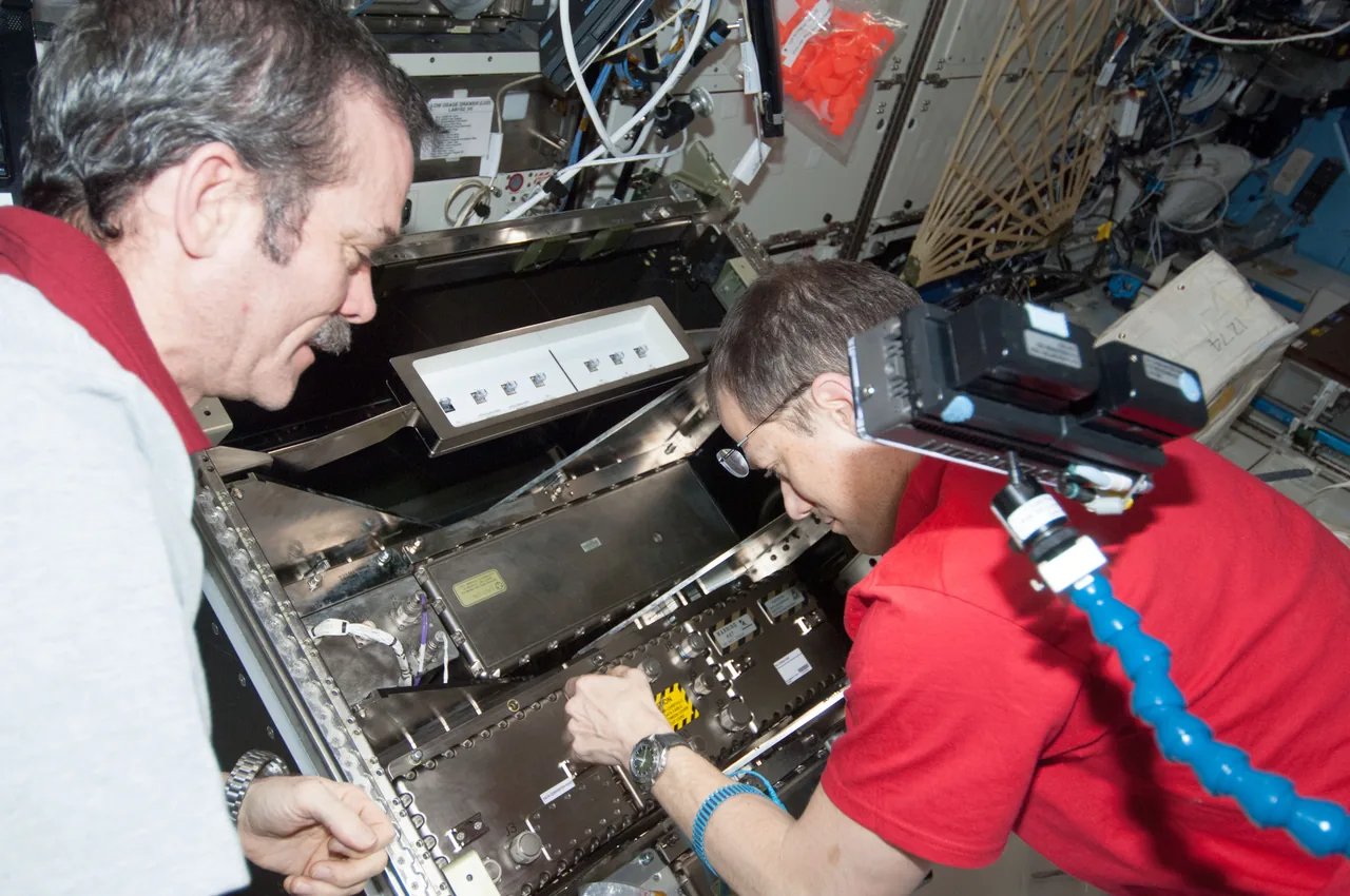 Chris Hadfield and Tom Marshburn working at an open communications equipment rack in Destiny