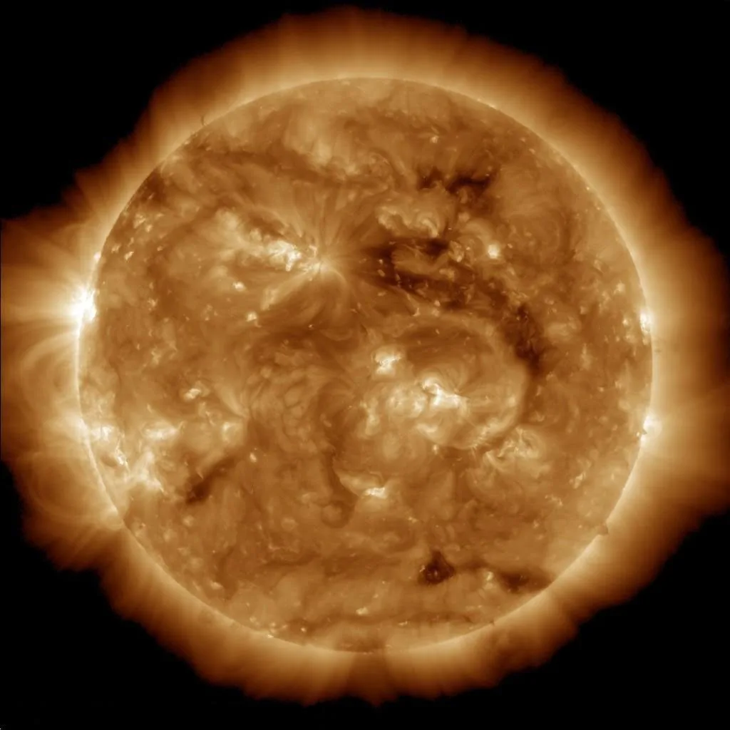 An orange extreme-ultraviolet view of the Sun with bright loops and an irregular darker patch above and right of center