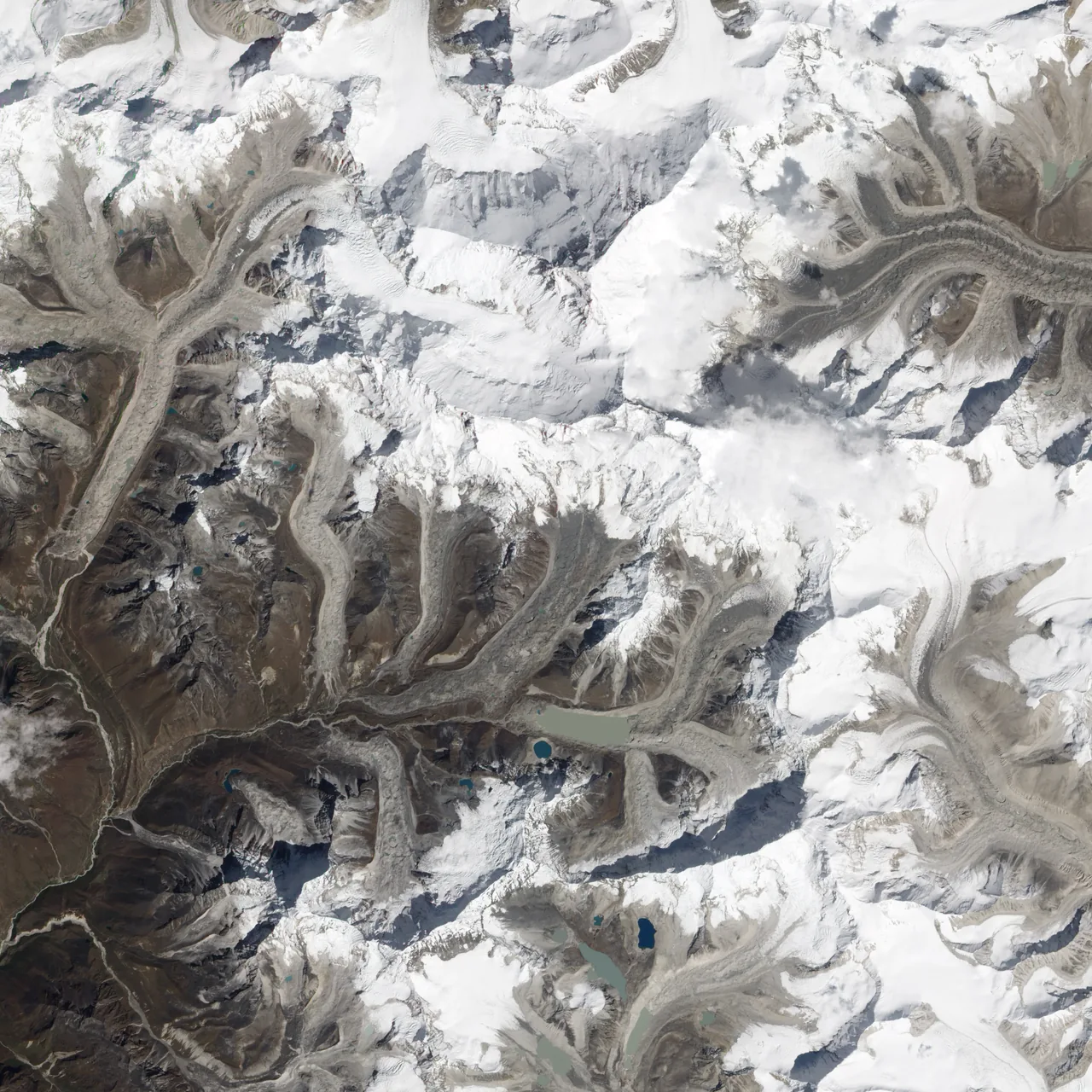 Natural-color satellite view of gray-brown Imja Tsho amid debris-covered glaciers, snowy mountains and dark terrain shadows in Nepal