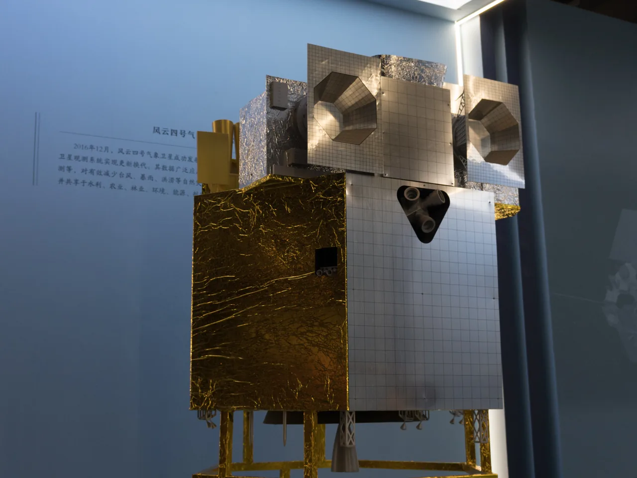 A gold-and-silver Fengyun-4 exhibit model with instrument openings and antennas, displayed on a stand in a museum.