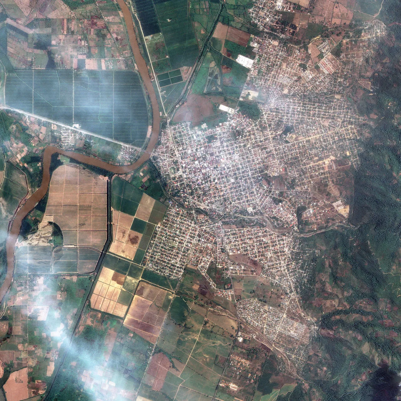 A satellite image shows a winding river, fields, roads and a town near Honduras’s Democracy Bridge