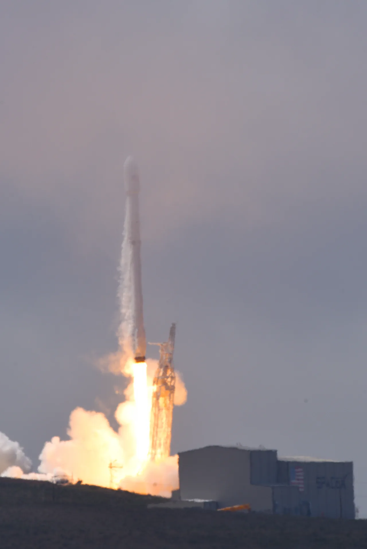 A Falcon 9 rises above its launch pad with a bright exhaust plume and vapor around the vehicle