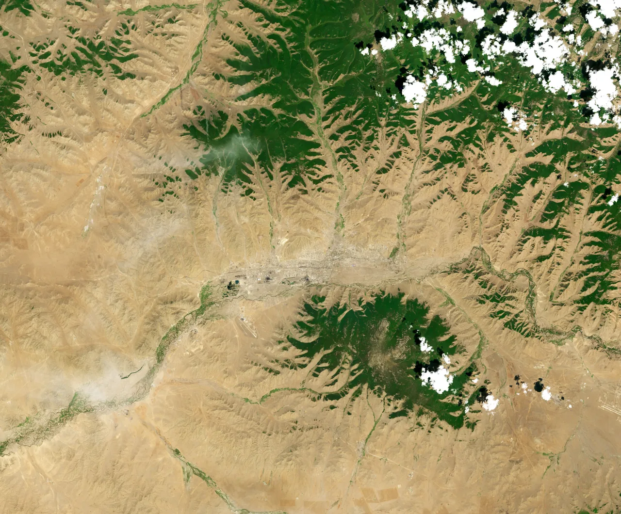 Natural-color orbital view of Ulaanbaatar in 2000, showing the city, river valleys, tan hills and dark-green forested slopes