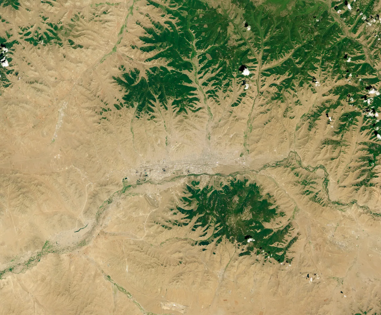 Natural-color orbital view of Ulaanbaatar in 2018, showing the city, river valleys, tan hills and dark-green forested slopes