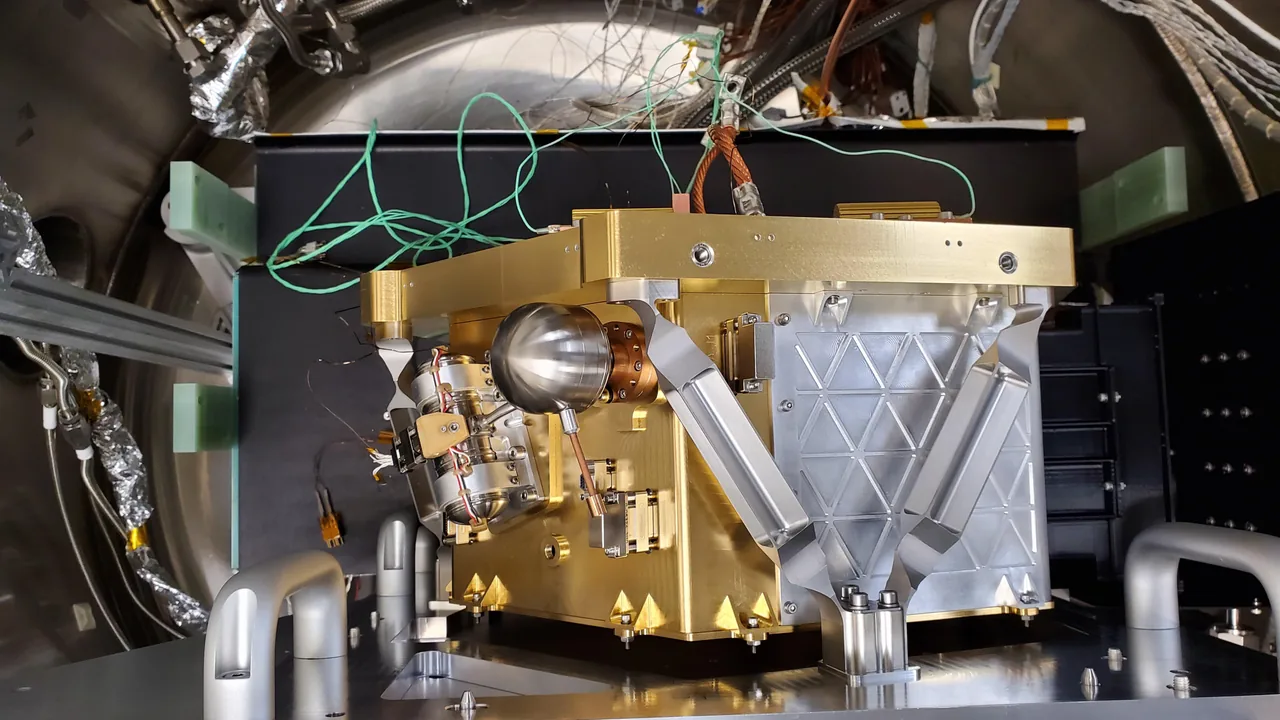 Gold-and-silver HVM3 instrument mounted inside a curved metal test enclosure, with attached cables and laboratory supports.