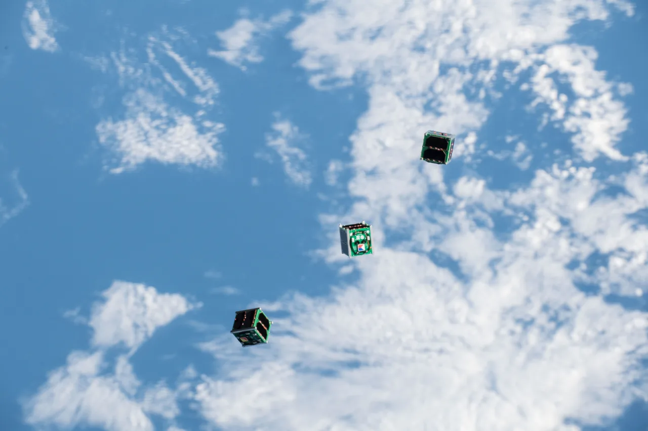 Three small box-shaped satellites drift above blue ocean and white clouds