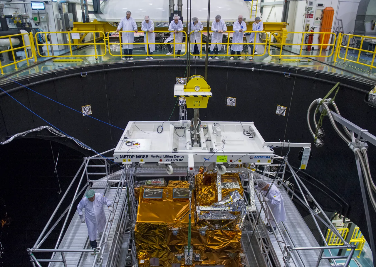 The insulated Metop-C payload module is suspended beneath lifting equipment inside a large test chamber