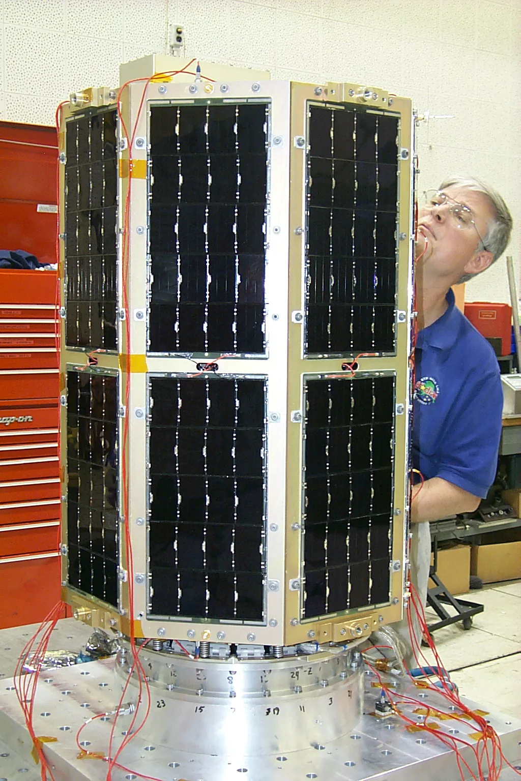 A solar-cell-covered MidStar 1 spacecraft stands in a laboratory with a person inspecting its side