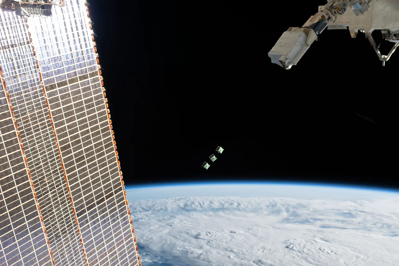 Three BIRDS-3 CubeSats float above Earth beside an International Space Station solar array and deployment equipment