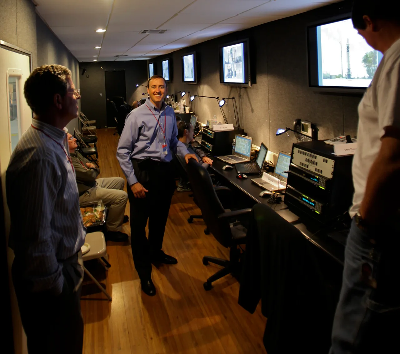 People stand and sit beside computer consoles and wall displays in a compact SpaceX control room