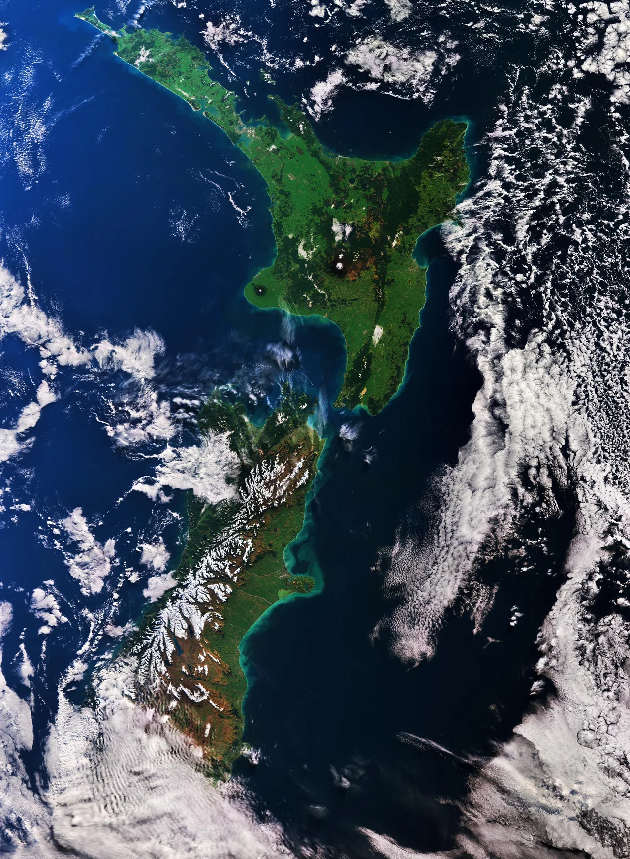 New Zealand’s North Island and much of the South Island, with snow-covered mountains, green land, coastal water and clouds