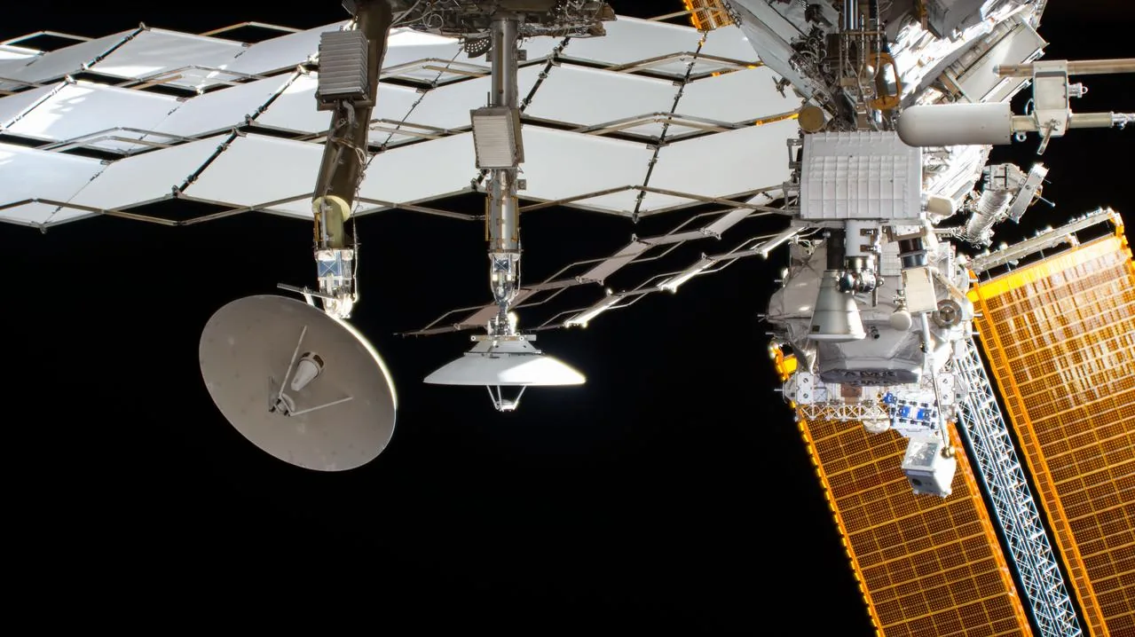 An external camera view shows station radiators, a solar array and mounted scientific equipment
