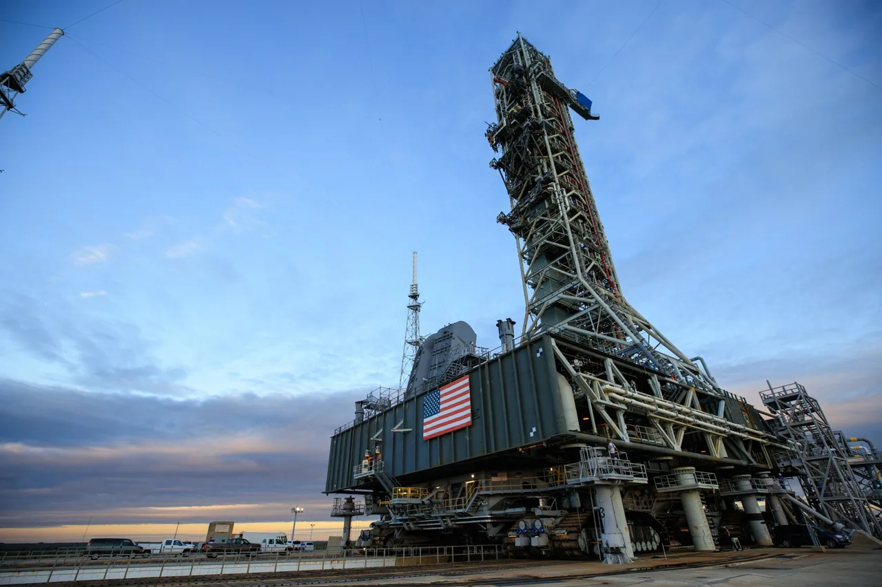 A tall launch tower and platform sit on a crawler-transporter under a blue sky