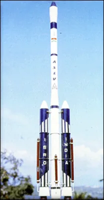 A slender white rocket configuration with two dark side boosters stands against a blue sky and trees.