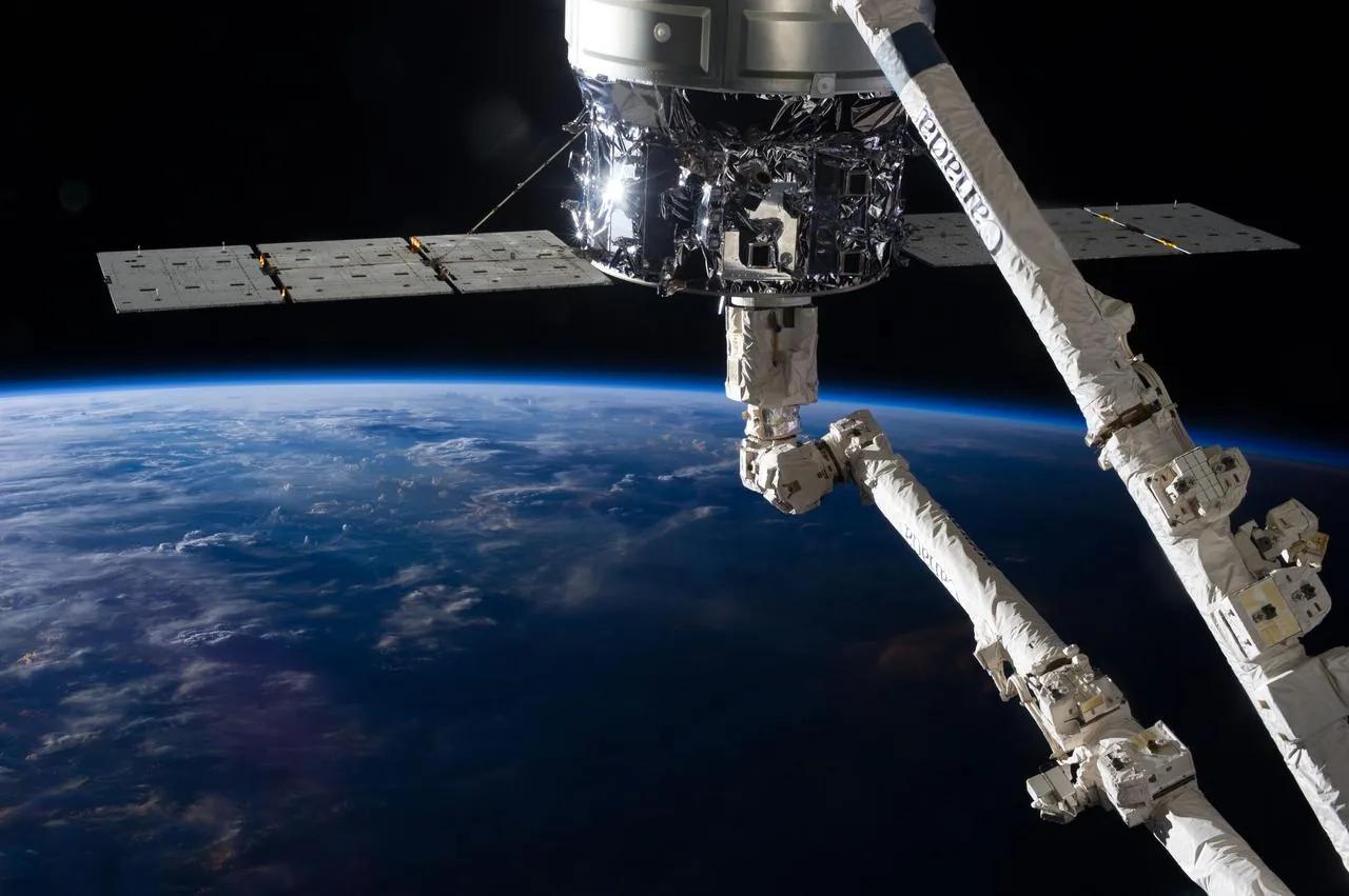 A white articulated robotic arm and Cygnus cargo spacecraft appear above the curved blue Earth