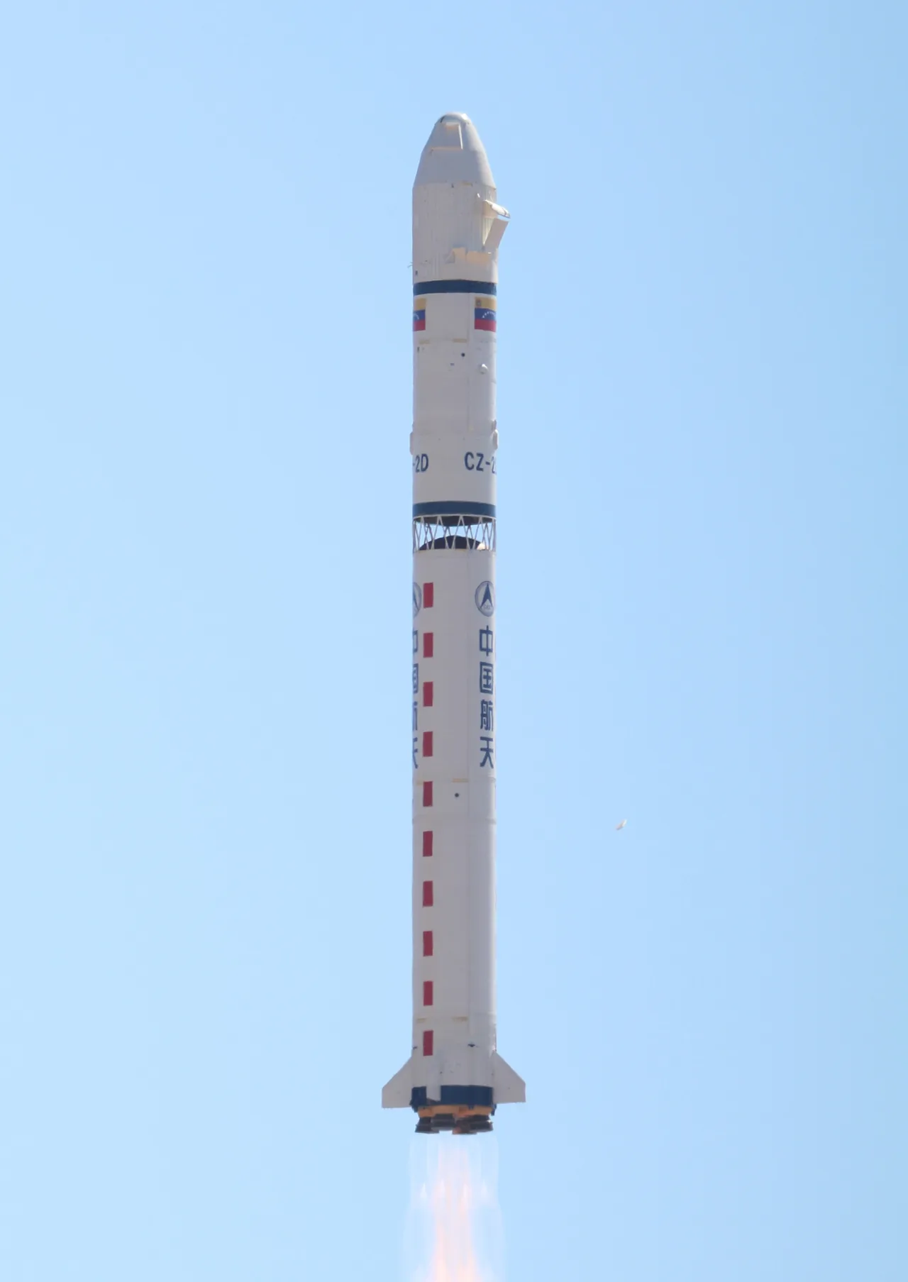 Long March 2D carrying Miranda rises above the launch site, with Venezuelan and Chinese flags visible on the white vehicle.