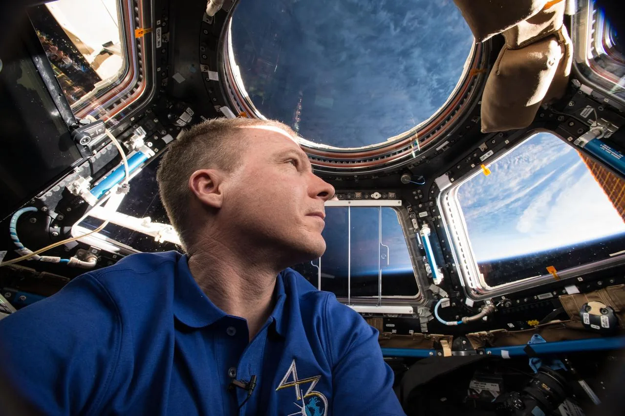 Terry Virts in a blue shirt photographs himself inside the station’s windowed Cupola with Earth visible outside
