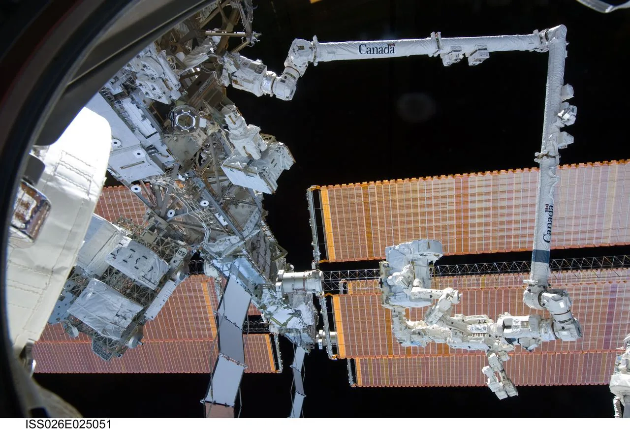 Dextre attached to Canadarm2 outside the space station, with solar arrays and station structure behind the robots
