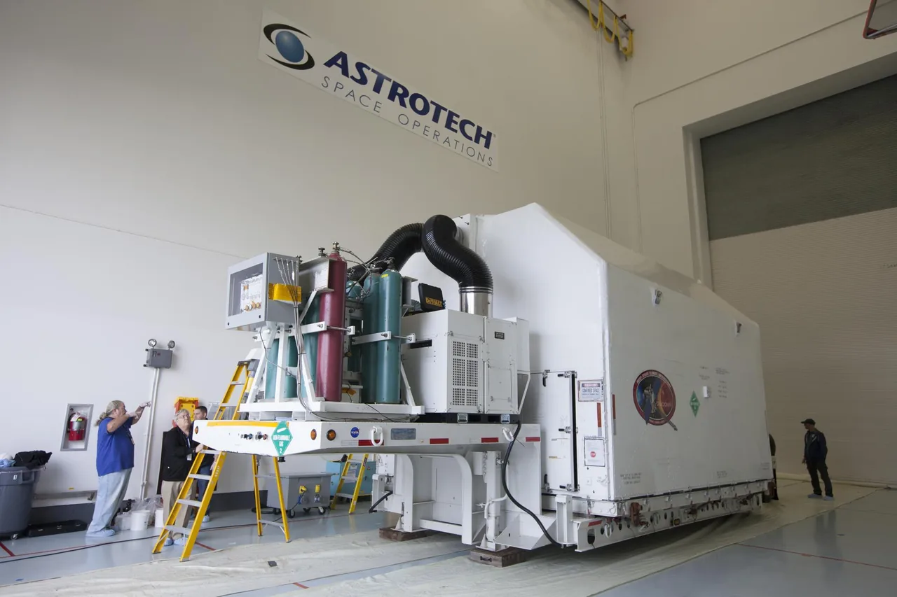 Workers prepare a large protective shipping enclosure inside an Astrotech facility