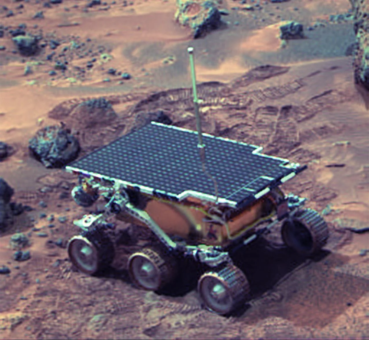 Sojourner stands on reddish Martian terrain with wheel tracks behind it and small rocks around the rover.