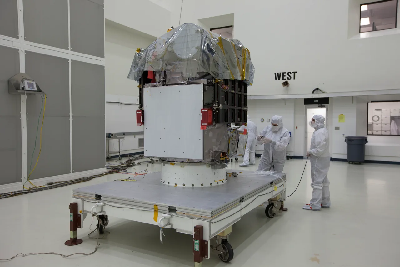 The DSCOVR flight spacecraft on a processing stand, with a transparent cover over its upper section and clean-room personnel at right.
