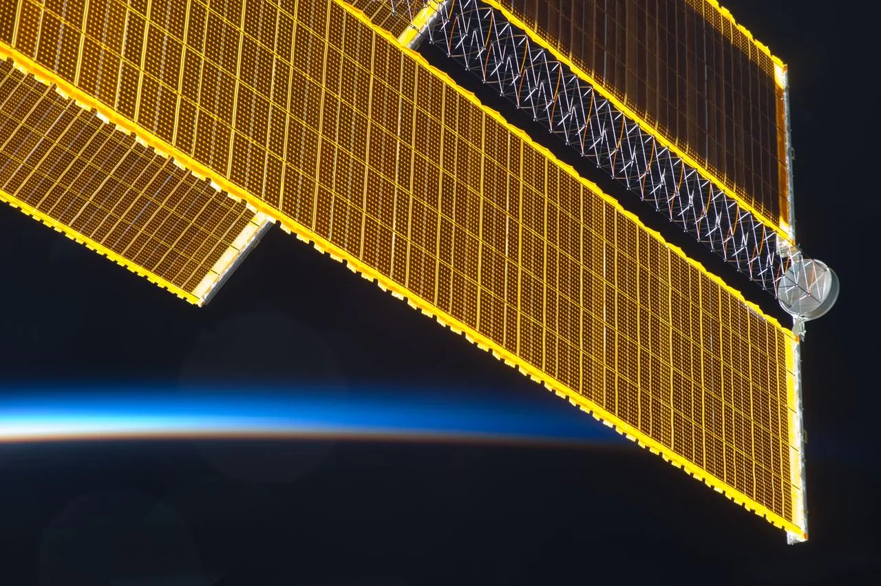 Golden station solar-array panels and their supporting mast above Earth’s thin blue horizon