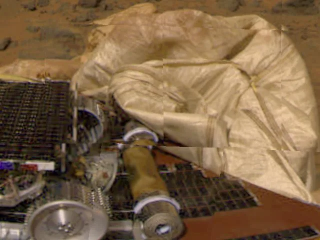 A partial Sojourner rover and rolled deployment ramp lie in front of pale landing airbags in the released Pathfinder color view.