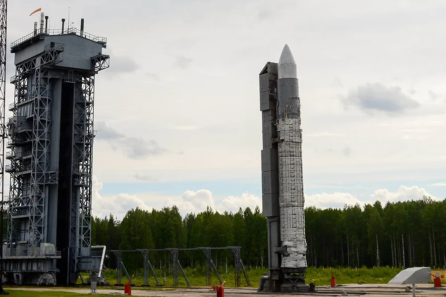 A white Rokot rocket beside a tall steel service structure with forest behind the pad