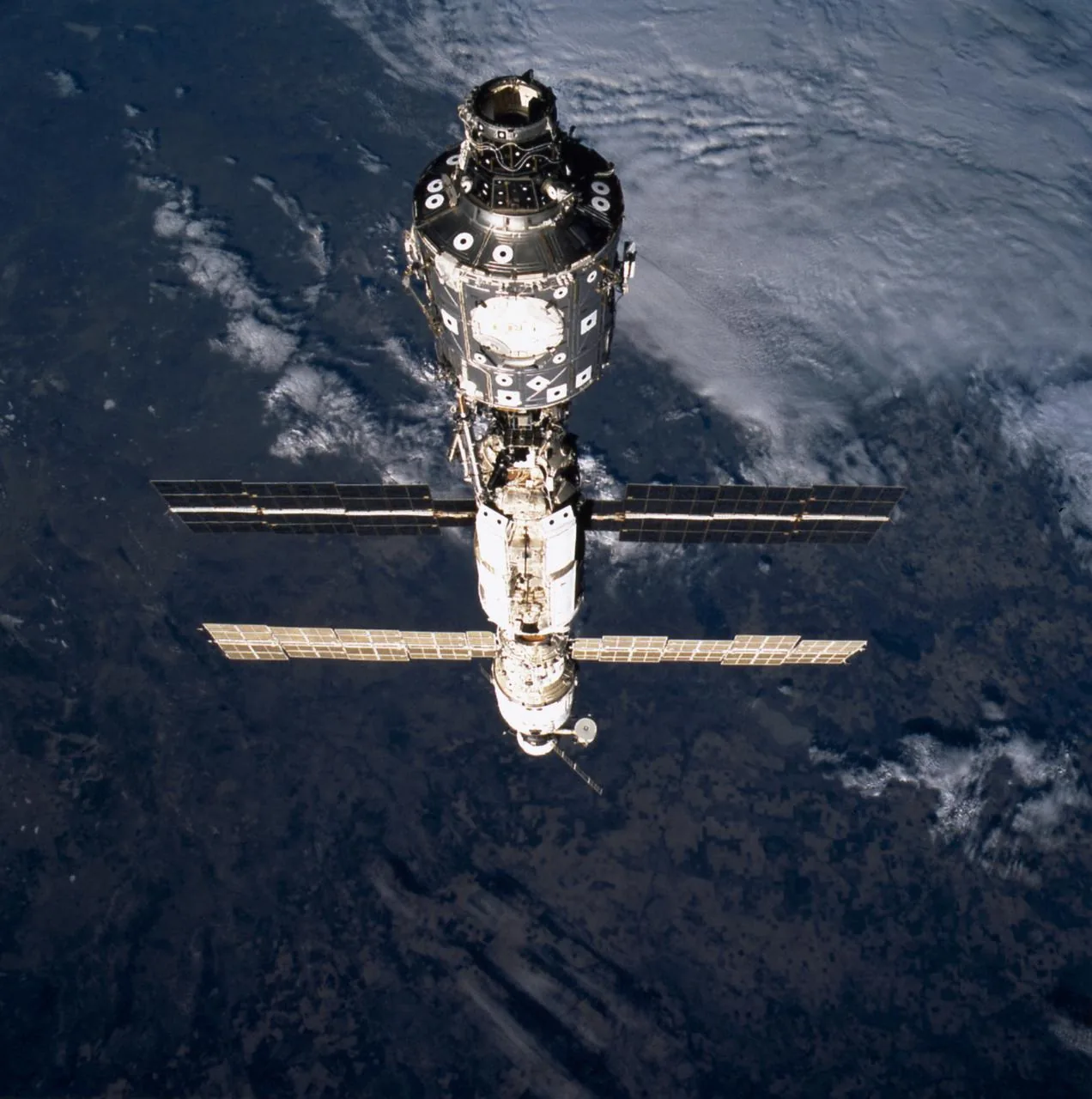 An early station configuration extends away from the nearest connecting module, with solar arrays crossing the view above Earth